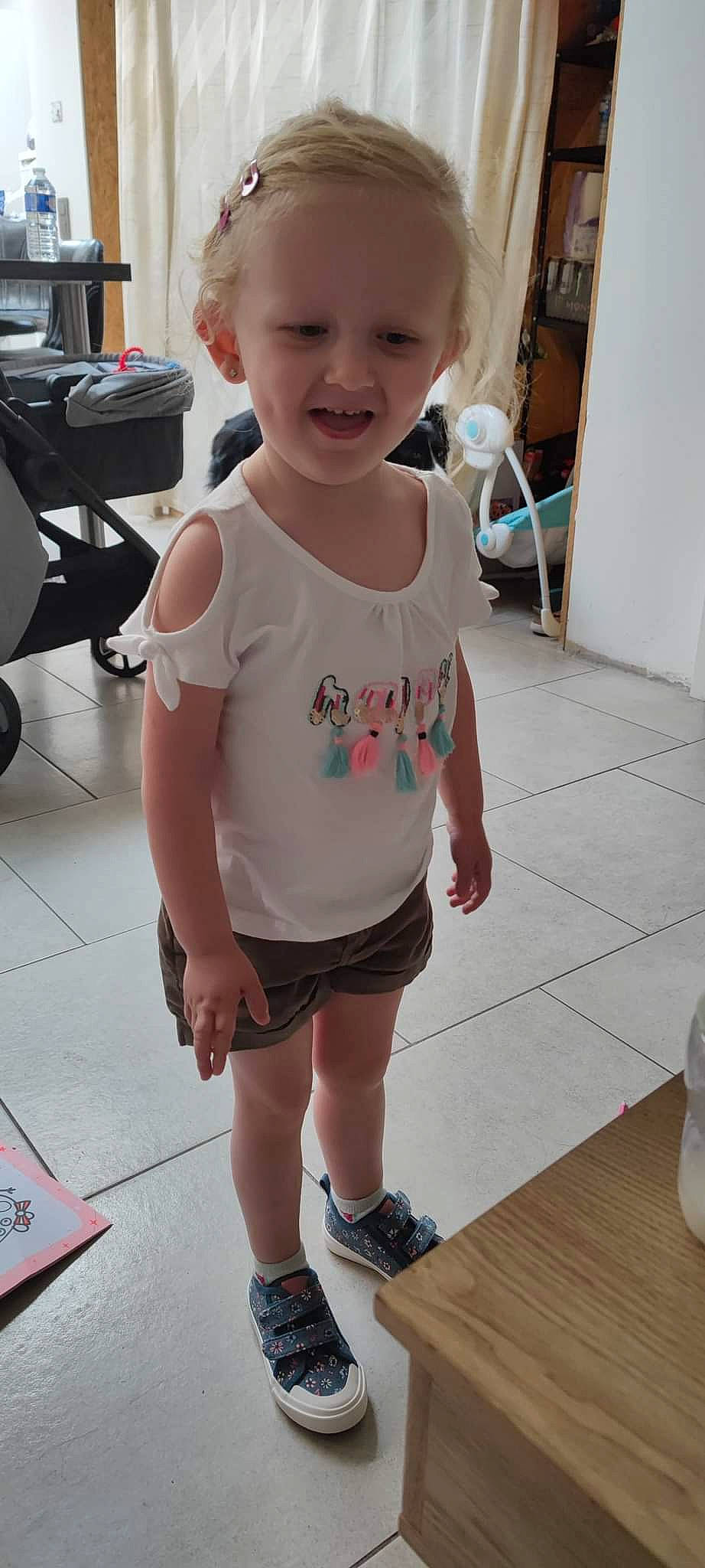 Siloé a rejoint le concours — aidez-le/la à gagner de superbes lots ! baby_toddler_clothing, cheek, chin, eye, face, floor, hair, joint, knee, leg, neck, person, shorts, skin, sleeve, smile, sportswear, standing, thigh, toddler