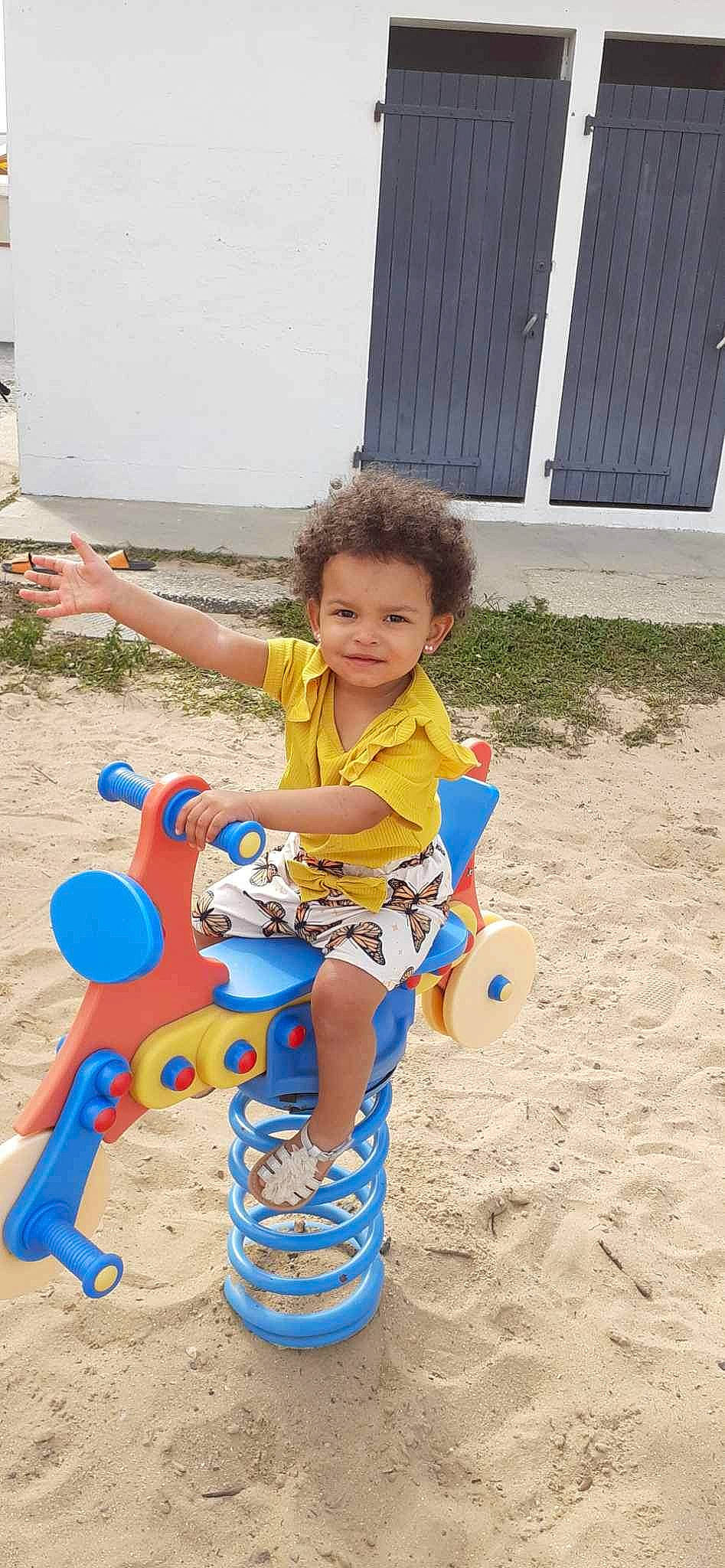 Yüna participe au concours pour gagner de l'argent avec cette photo : baby_toddler_clothing, child, city, door, electric_blue, fun, happy, joy, landscape, leisure, outdoor_play_equipment, person, play, recreation, sand, sitting, smile, soil, t_shirt, toddler