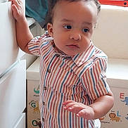 Aziah is registered to the contest to win money with this photo: toddler, child, striped_shirt, curly_hair, indoor, furniture, drawer, alphabet_wall, animal_illustrations, colorful, casual_clothing, young_child, standing, hand_on_drawer, looking_away, playful_background, cozy, portrait, home, cute
