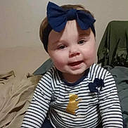 Starla is registered to the contest to win money with this photo: baby, child, headband, bow, striped_shirt, golden_bear, smiling, face, indoor, bed, blanket, clothing, seated, cute, young_child, portrait, happy, person, casual, infant