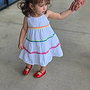Valentina is registered to the contest to win money with this photo: child, girl, white_dress, rainbow_stripes, red_shoes, holding_hands, adult_hand, sidewalk, outdoor, curly_hair, portrait, standing, casual, cute, person, fashion, summer, smile, young, background_blur