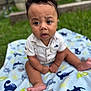 Haelo is registered to the contest to win money with this photo: baby, infant, child, blanket, dinosaur_pattern, outdoor, grass, curly_hair, expression, clothing, cute, sitting, foot, hand, portrait, young, skin, nature, daylight, person