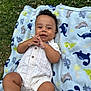 baby, child, smile, blanket, dinosaur_pattern, grass, outdoor, infant, clothing, cute, portrait, happy, lying_down, young_child, skin, head, hand, foot, nature, playful