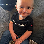 Carson joined the competition — help win amazing prizes! toddler, child, smile, jeans, black_tshirt, champion_logo, couch, blanket, indoor, cozy, cute, portrait, person, sitting, happy, young_child, casual_clothing, home, baby, face