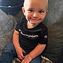 toddler, child, smile, jeans, black_tshirt, champion_logo, couch, blanket, indoor, cozy, cute, portrait, person, sitting, happy, young_child, casual_clothing, home, baby, face