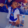 toddler, child, chair, hand, wall_mural, animated_characters, blue_shirt, white_jacket, sneakers, indoor, person, standing, colorful_background, holding_hand, smiling, shorts, fashion, cute, portrait, playful