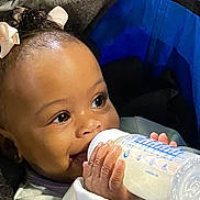 Truee joined the competition — help win amazing prizes! baby, bottle, milk, child, cute, face, hand, hair_bow, infant, milk_bottle, person, portrait, sitting, smiling, feeding, closeup, young_child, happy, indoors, skin