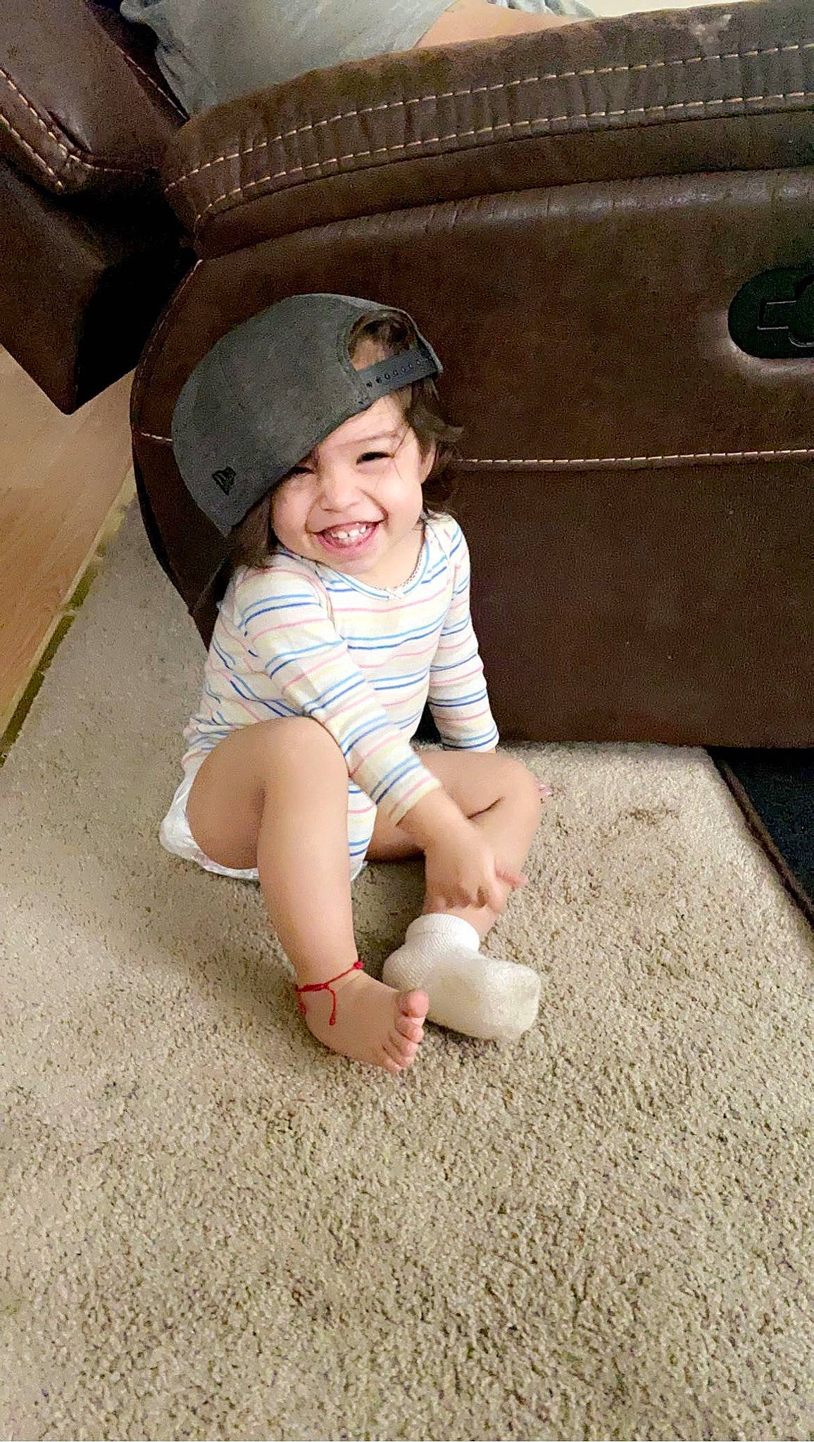 Zaniyah is registered to the contest to win money with this photo: automotive_tire, baby_toddler_clothing, baseball_cap, cap, comfort, eye, floor, flooring, foot, grass, head, headgear, headwear, human_body, joy, knee, leg, person, skin, sleeve