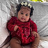 baby, bows, child, chubby_cheeks, couch, cozy, curly_hair, cute, home, indoor, infant, person, plush, portrait, quilted, red_dress, relaxing, sitting, smiling, soft_light