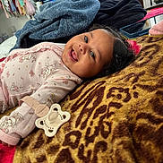 Alani joined the competition — help win amazing prizes! baby, blanket, casual, child, clothing, curly_hair, face, furniture, happy, home, indoors, lying_down, pacifier, pacifier_clip, patterned_blanket, person, pink, room, smiling, television