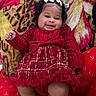 Alani joined the competition — help win amazing prizes! baby, blanket, bow, child, cozy, curly_hair, cute, face, fashion, happy, indoors, infant, pattern, person, plush, portrait, red_dress, sitting, smiling, toddler