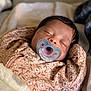 baby, sleeping, pacifier, blanket, floral_pattern, pink_clothing, infant, cute, peaceful, cozy, child, portrait, indoors, soft_texture, newborn, resting, closeup, head, face, hands_up