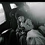 child, car_seat, winter_hat, jacket, blanket, snack, car_interior, window, seatbelt, young_child, monochrome, portrait, indoors, cozy, casual, seat, person, child_seat, travel, window_light