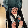 baby, child, stroller, cap, smile, happy, indoor, clothing, seatbelt, person, footwear, socks, cute, infant, cheerful, face, headwear, seated, baby_toy, expression