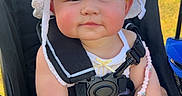 Emily Sophia is registered to the contest to win money with this photo: baby, child, stroller, white_hat, pacifier, outdoor, sunny_day, flower, face, smiling, cute, seatbelt, summer_clothing, person, infant, pink_cheeks, relaxed, sitting, nature, daylight