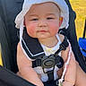 baby, child, stroller, white_hat, pacifier, outdoor, sunny_day, flower, face, smiling, cute, seatbelt, summer_clothing, person, infant, pink_cheeks, relaxed, sitting, nature, daylight