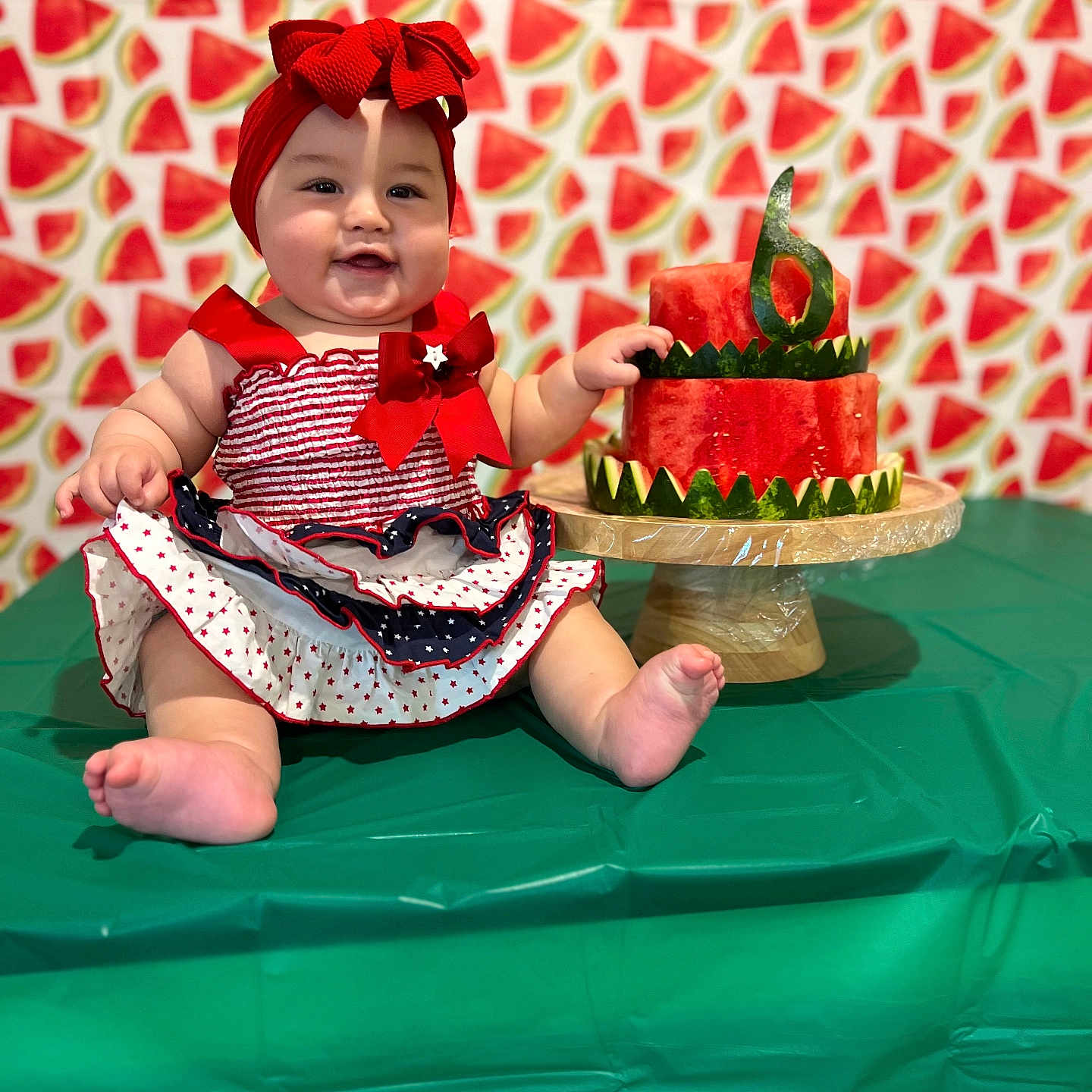 Emily Sophia is registered to the contest to win money with this photo: baby, child, birthday, watermelon, cake, red_bow, headband, dress, table, green_tablecloth, smile, face, cheeks, celebration, background_pattern, food, fruit, number_six, festive, sitting