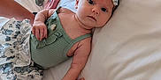 Sosie joined the competition — help win amazing prizes! baby, infant, child, hand, bed, white_bed, bow, headband, green_top, floral_skirt, person, skin, fingers, lying_down, indoors, soft_light, adult_hand, curious, cute, portrait