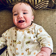 Matthew is registered to the contest to win money with this photo: baby, infant, smile, laughing, pajamas, giraffe_pattern, hand, cheeks, hair, sofa, cushion, upholstery, portrait, close_up, eyes, mouth, skin, cozy, home, cute