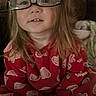 child, glasses, pajamas, heart_pattern, red_clothing, sitting, indoors, couch, blanket, cozy, curly_hair, face, person, comfort, playful, smiling, young, cute, home, soft