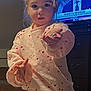 child, toddler, pajamas, heart_pattern, ponytail, messy_hair, offering_hand, rock, television, news_broadcast, tv_presenter, indoor, bedroom, bed_rail, dresser, expression, portrait, cute, soft_lighting, clothing
