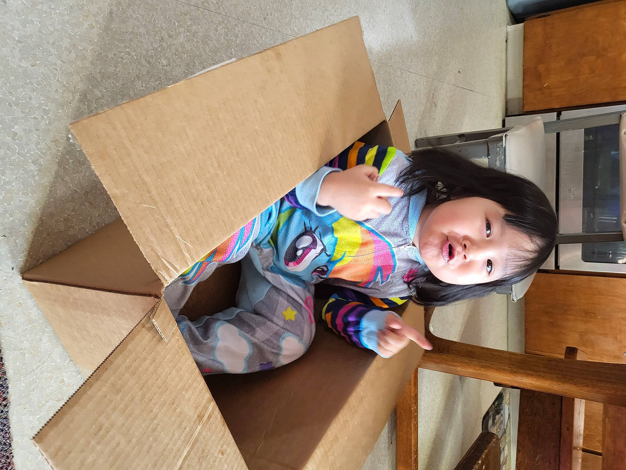Helena is registered to the contest to win money with this photo: baby_toddler_clothing, cardboard, carton, child, flooring, hardwood, home_appliance, house, kitchen_appliance, packaging_and_labeling, paper, paper_product, person, room, shipping_box, sitting, sleeve, suit, t_shirt, toddler