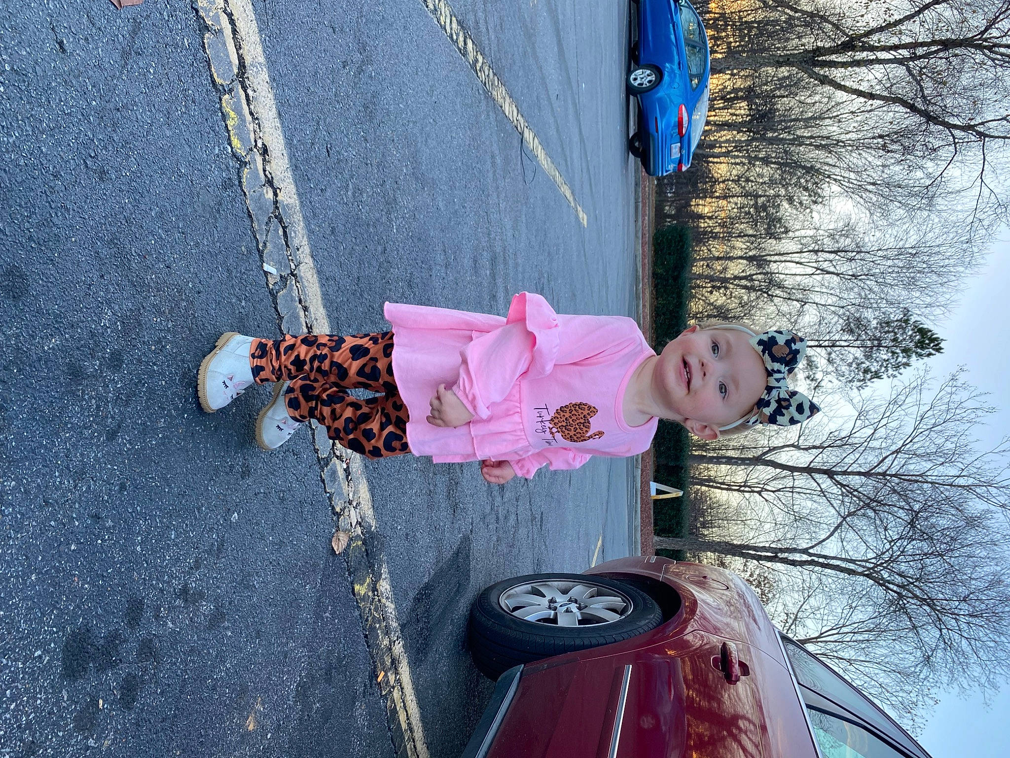 Jacklyn is registered to the contest to win money with this photo: asphalt, automotive_lighting, blue, car, headwear, joy, line, motor_vehicle, person, photograph, pink, plant, road_surface, sidewalk, sky, smile, textile, tire, toddler, tree