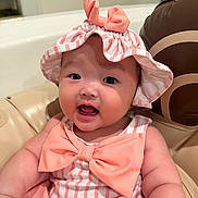 Rosee joined the competition — help win amazing prizes! baby, child, infant, pink, hat, bow, smile, cute, face, chubby_cheeks, striped_clothing, sitting, indoors, seat, cushion, portrait, happy, headwear, person, closeup