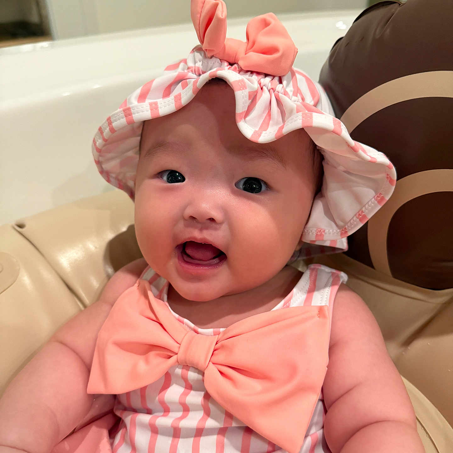 Rosee joined the competition — help win amazing prizes! baby, bow, child, chubby_cheeks, closeup, cushion, cute, face, happy, hat, headwear, indoors, infant, person, pink, portrait, seat, sitting, smile, striped_clothing