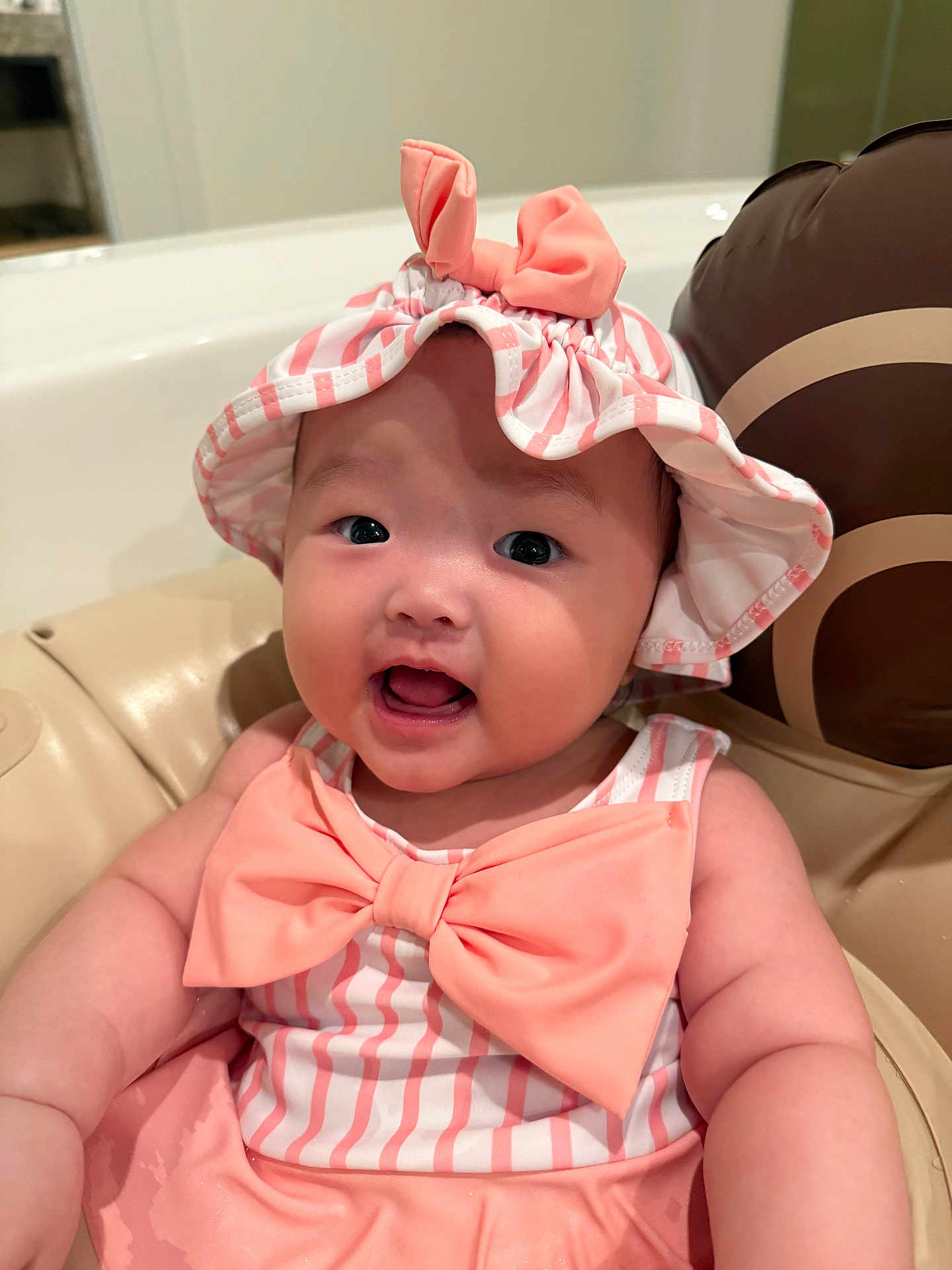 Rosee joined the competition — help win amazing prizes! baby, child, infant, pink, hat, bow, smile, cute, face, chubby_cheeks, striped_clothing, sitting, indoors, seat, cushion, portrait, happy, headwear, person, closeup