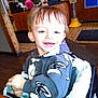 Charles is registered to the contest to win money with this photo: toddler, child, smile, face, indoor, high_chair, clothing, hoodie, person, wood, floor, tile, table, hand, hair, seat, happy, casual, restaurant, background