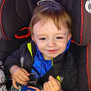 Charles is registered to the contest to win money with this photo: toddler, child, car_seat, seat_belt, blanket, keychain, flip_flop, blue_scarf, smile, face, hair, hand, clothing, toy, indoor, portrait, young_child, cozy, happy, baby