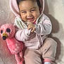 baby, smiling, hoodie, plush_toy, pink, cozy, cute, infant, happy, child, soft_texture, socks, flamingo, cuddly, portrait, indoors, clothing, relaxed, seated, toddler