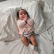 Azriella joined the competition — help win amazing prizes! baby, bed, blanket, child, cute, floral_shorts, hands_together, indoors, infant, knitted_cardigan, lying_down, person, pillow, portrait, relaxed, sleepwear, smiling, socks, soft_lighting, young