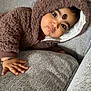 baby, child, hoodie, brown_clothing, couch, sofa, hand, face, curious, indoors, texture, fuzzy, cute, portrait, young_child, infant, comfortable, cozy, expression, casual