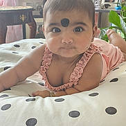 Merxin is registered to the contest to win money with this photo: baby, infant, child, face, pink_clothing, polka_dot, cushion, indoor, portrait, wide_eyes, curious_expression, ruffles, bracelet, plant, framed_photos, wooden_table, soft_light, home_interior, lying_down, black_dot