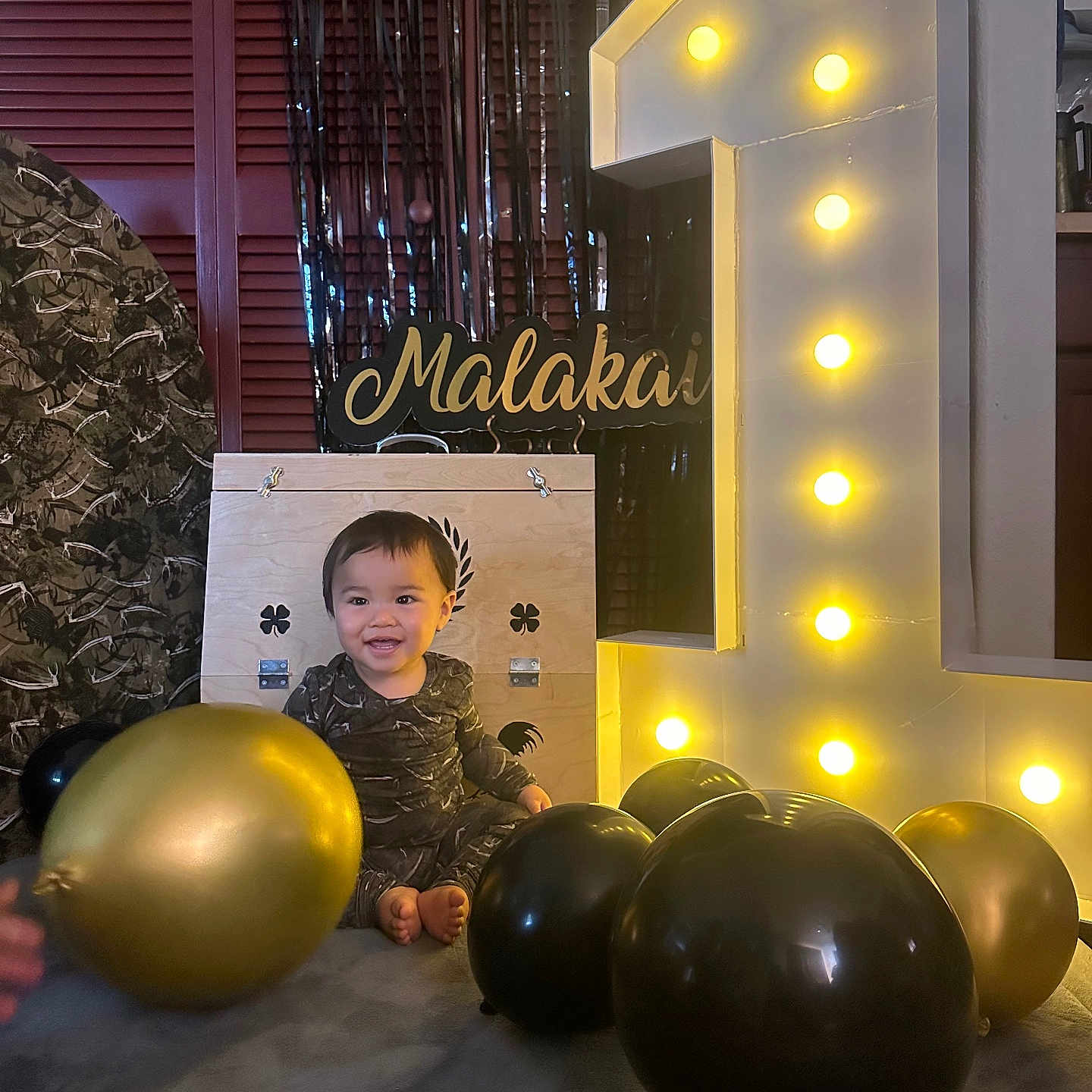 Malakai joined the competition — help win amazing prizes! toddler, child, balloon, black_balloon, gold_balloon, birthday, number_one, illuminated_number, wooden_box, smiling, indoor, celebration, party, happy, floor, clothing, face, person, decor, lighting
