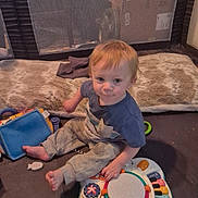 Samuel joined the competition — help win amazing prizes! toddler, child, toy, playpen, blanket, indoor, floor, musical_toy, clothing, sitting, baby, cute, face, light_hair, expression, curious, soft_toy, plastic_toy, carpet, home