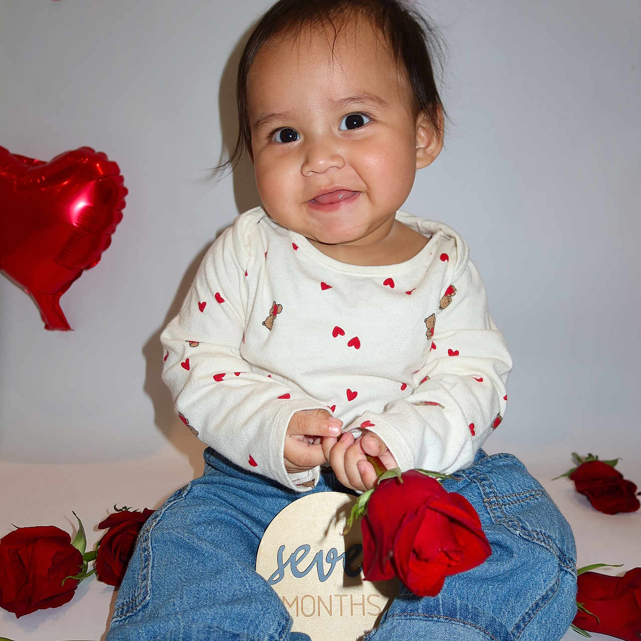 Damian joined the competition — help win amazing prizes! baby, balloon, barefoot, celebration, child, cute, heart_balloon, heart_pattern, indoor, jeans, long_sleeve_shirt, milestone, person, portrait, red_rose, rose, seven_months, sitting, smiling, white_background