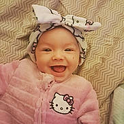 Raya is registered to the contest to win money with this photo: baby, smile, pink_clothing, hello_kitty, headband, bow, blanket, cute, infant, happy, face, child, apparel, pattern, lying_down, indoors, portrait, young_child, warm_clothing, cozy