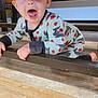 baby, child, crawling, onesie, heart_pattern, wooden_table, floor, indoor, wide_eyes, open_mouth, curious, person, furniture, wood_floor, playful, young_child, expression, hands, legs, candid