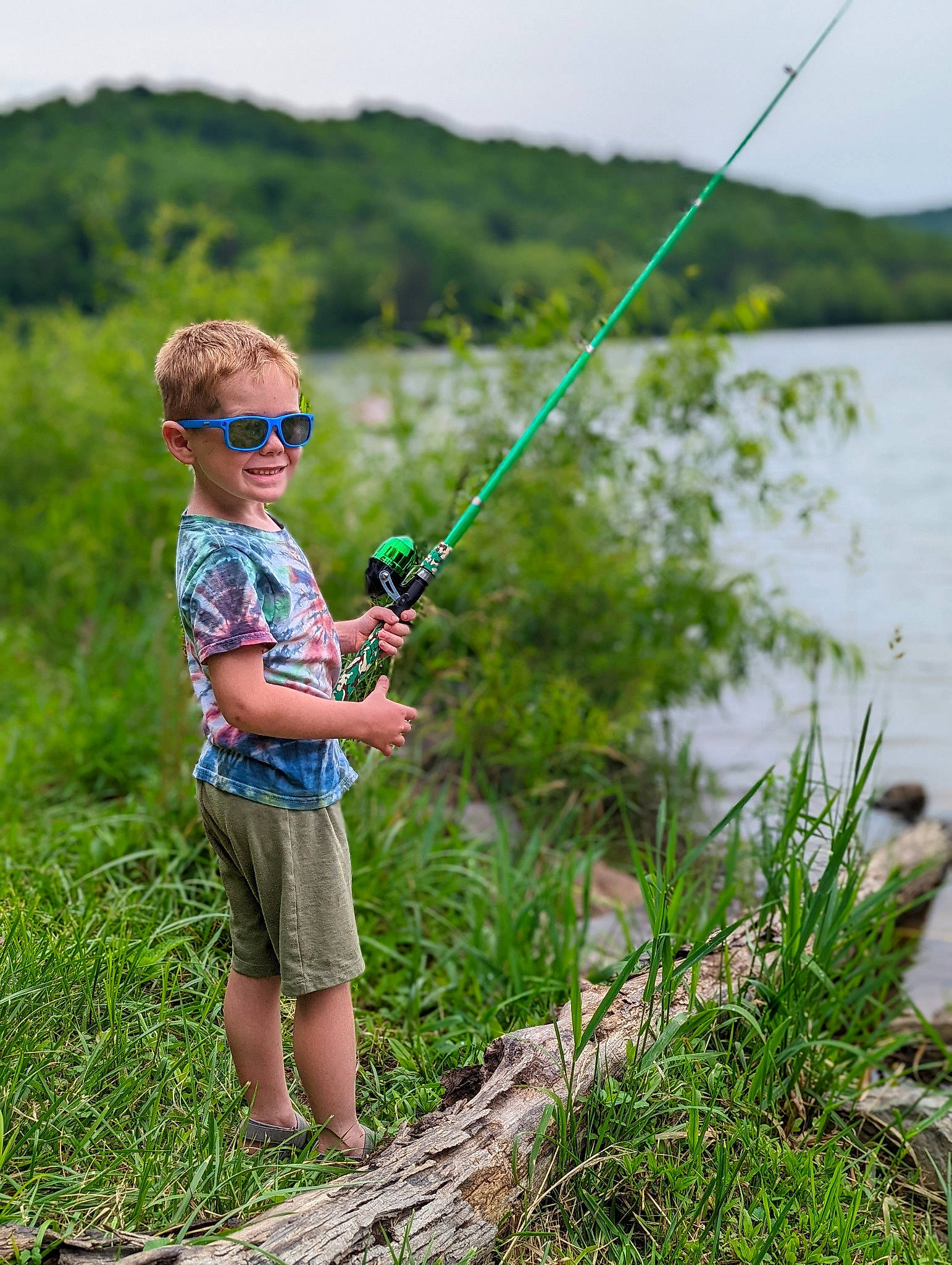 Keaton is registered to the contest to win money with this photo: angling, casting_fishing, fisherman, fishing, fishing_reel, fishing_rod, fun, grass, grassland, lake, leisure, people_in_nature, person, plant, recreational_fishing, shorts, sky, summer, sunglasses, toddler