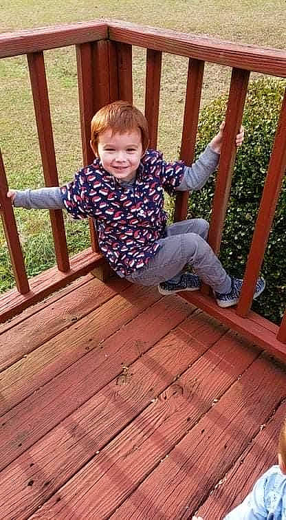 Jaden is registered to the contest to win money with this photo: baby_toddler_clothing, composite_material, deck, flooring, fun, grass, happy, hardwood, joy, leisure, pattern, person, plank, shorts, sitting, smile, t_shirt, toddler, varnish, wood