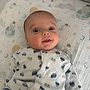 Eden a rejoint le concours — aidez-le/la à gagner de superbes lots ! baby, infant, onesie, crib, face, smile, eyes, clothing, bed, blanket, pattern, space_theme, cars, cute, child, portrait, indoors, laying_down, young, person