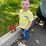 child, boy, yellow_shirt, toy_dinosaur, sidewalk, curb, grass, car, parking_lot, outdoor, sunlight, jeans, shoes, smile, nature, tree, play, summer, casual, daytime