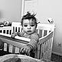 baby, crib, child, indoor, monochrome, person, hand, face, curly_hair, expression, bedroom, door, blanket, toy, wall, carpet, long_sleeve, furniture, infant, looking