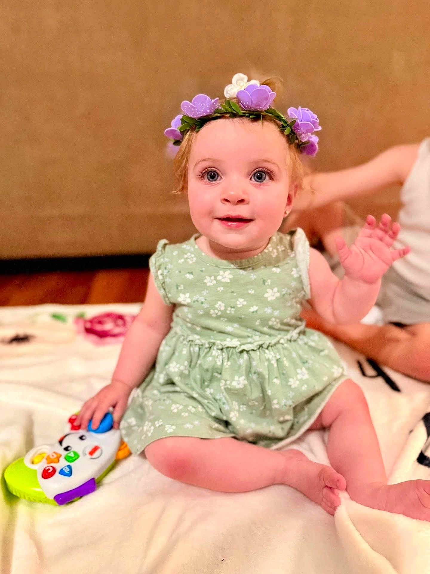 Coralie joined the competition — help win amazing prizes! baby, child, girl, flower_crown, green_dress, toy, piano_toy, blanket, smiling, waving_hand, indoor, floor, cute, sitting, happy, playful, person, young_child, headwear, soft_lighting
