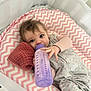 Coralie is registered to the contest to win money with this photo: baby, bottle, crib, pink, chevron_pattern, blue_eyes, blanket, clothing, infant, feeding, sleeping_area, soft_toy, child, indoors, cute, hand, face, sleepwear, resting, young
