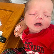 Elijah Davis joined the competition — help win amazing prizes! newborn, baby, infant, sleeping, red_shirt, hand, plaid_pants, wooden_table, remote_control, closeup, person, child, resting, cute, indoors, comfort, shirt, holding, peaceful, portrait