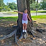 child, girl, tree, tree_root, outdoor, grass, sidewalk, street, sign, smile, summer, sunlight, clothing, shoes, nature, daytime, balance, pose, happy, park